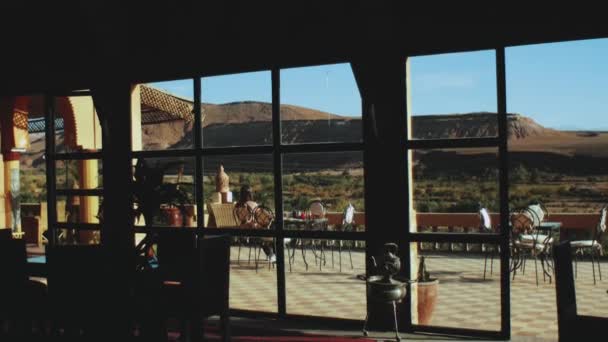 Γυναίκα έχουν παραδοσιακό πρωινό στη βεράντα του Μαρόκου Ριάντ με όμορφη θέα στην έρημο βράχους, άποψη από πανοραμικό παράθυρο, πλήρως hd — Αρχείο Βίντεο