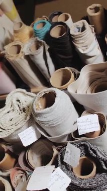 Dikey video. Mobilya fabrikasında raflara dizilmiş kumaş ve tekstil ruloları. Depoya yakın çekim, çeşitli kumaşlar, yavaş çekim. Yüksek kalite 4k görüntü