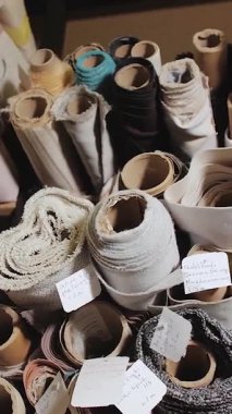 Kumaş ve tekstil ruloları mobilya fabrikasının raflarına istiflenmiş mobilya dikiş ekipmanları deposunda yatıyor. Depoya yakın çekim, çeşitli kumaşlar. Dikey video. Yüksek kalite 4k