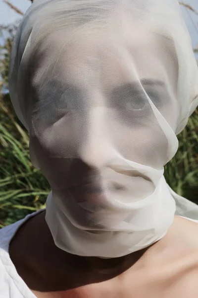 girl hidden white veil walks on a field.unusual bride