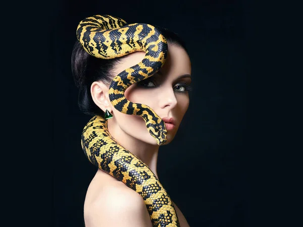 beautiful young woman with Snake on her head like a hair. Brunette model with fashion make up. Beauty close up studio shot.jewelry earrings