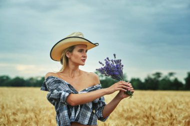 Buğday alanıyla bir yürüyüş için rahat kıyafetler genç kadın. Çiçekli lavanta tutan kız