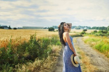 Buğday alanında bir yolda hafif yaz elbiseli Genç romantik kadın