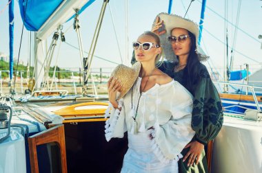 İki genç çekici kadın güneşli bir günde bir yatta dinlenme. Güzel kadınlar bir yatta moda yaz giysileri