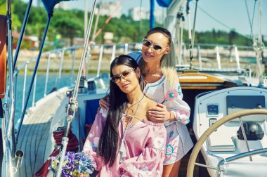 İki genç çekici kadın güneşli bir günde bir yatta dinlenme. Güzel kadınlar bir yatta moda yaz giysileri