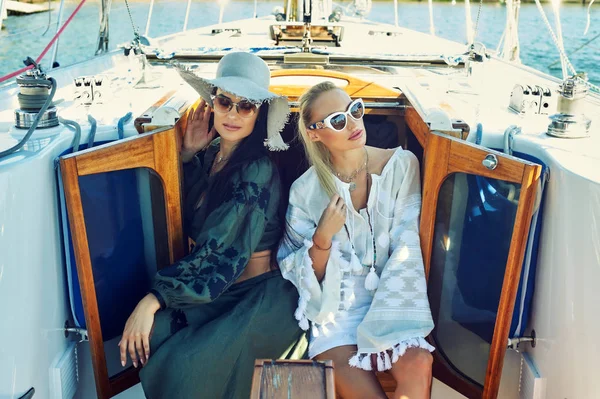 İki genç çekici kadın güneşli bir günde bir yatta dinlenme. Güzel kadınlar bir yatta moda yaz giysileri