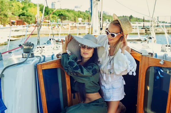 İki genç çekici kadın güneşli bir günde bir yatta dinlenme. Güzel kadınlar bir yatta moda yaz giysileri