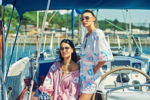 İki genç çekici kadın güneşli bir günde bir yatta dinlenme. Güzel kadınlar bir yatta moda yaz giysileri