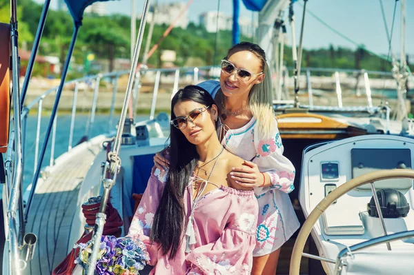 İki genç çekici kadın güneşli bir günde bir yatta dinlenme. Güzel kadınlar bir yatta moda yaz giysileri