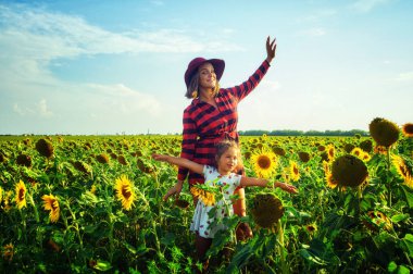Yaz aylarında açık havada sevgi dolu aile mutlu. Genç Anne ve gülüyor ve ayçiçeği alanıyla oynayan kız