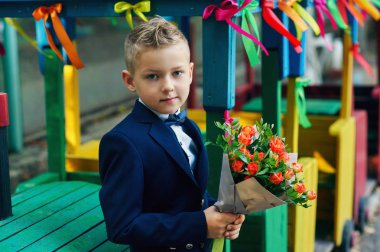 Bir buket çiçek güzel çocuk. Bir çiçek tutan bir birinci sınıf öğrencisi. Takım elbiseli şık çocuk
