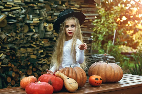 The Holiday Of Halloween! Cute little girl with pumpkins. Beautiful young baby girl in witch costume outdoors.