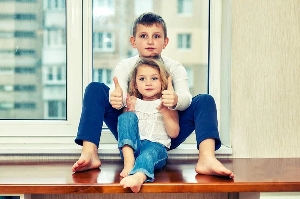一个小女孩和一个弟弟坐在房子的窗台上的肖像 — 图库照片