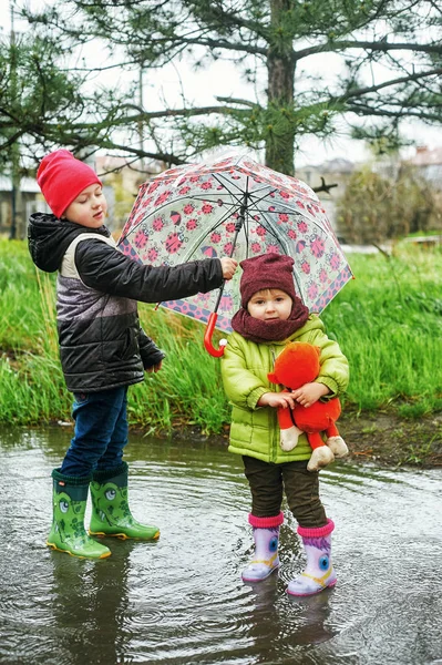 Portrait of brother and sister on a walk in the rain . Children walk with an umbrella