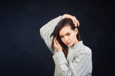 Stüdyo karanlık bir arka plan üzerinde genç bir kadın portresi. Kız sıcak bir örme Kazak giymiş