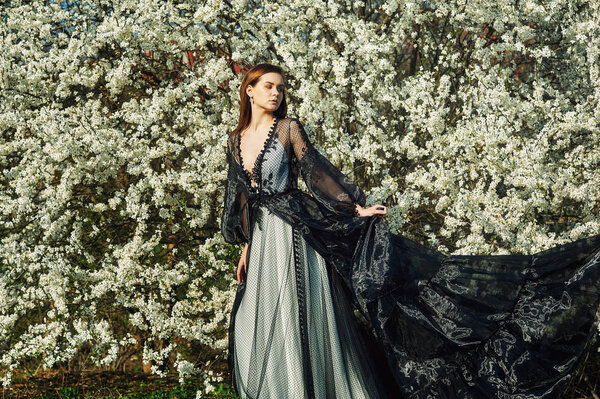 Portrait of a young beautiful fashionable woman in an evening dress . Girl posing in a blooming garden