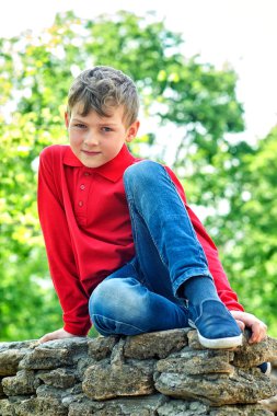 Şehir parkındaki bir çocuğun açık portresi. Çocuk kot pantolon ve kırmızı bir tişört giyiyor.