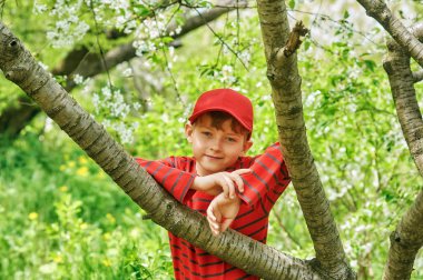 Bahar parkındaki bir çocuğun portresi. Çocuk bir şapka ve kırmızı bir tişört giyiyor.