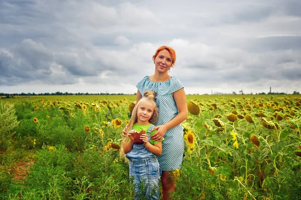 Funny mom and daughter on a walk in the field with sunflowers