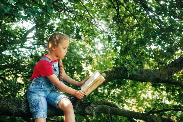 Little blonde girl with a book on a tree . Children\'s out-of-school education