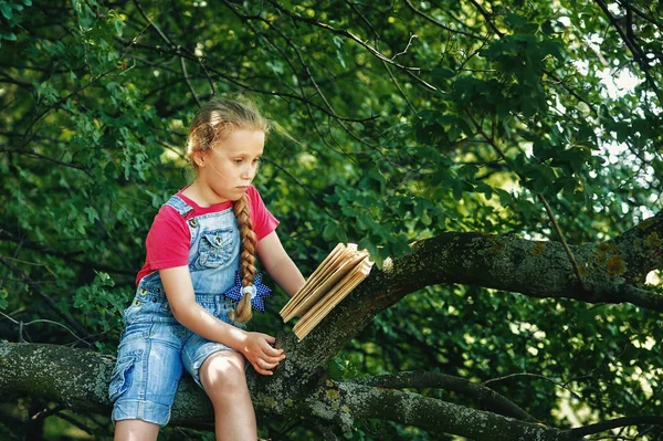 Little blonde girl with a book on a tree . Children's out-of-school education