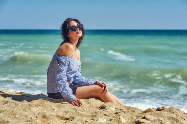 Beautiful young healthy girl in fashionable sunglasses at the seaside . The model wears a blouse and skirt