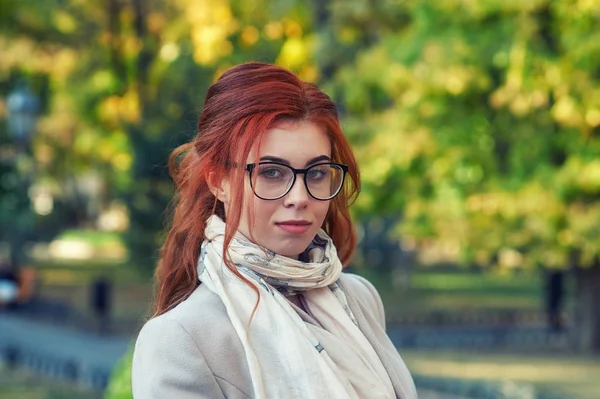 秋の都市公園で若い女性の肖像画 ベージュのコートを着た赤い髪の女の子 ストック画像