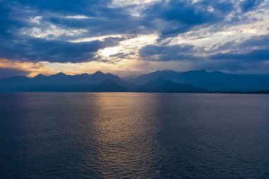 Güzel gün batımı bulutlu gökyüzü ve karanlık deniz suyu Dağları'nın siluetleri ile