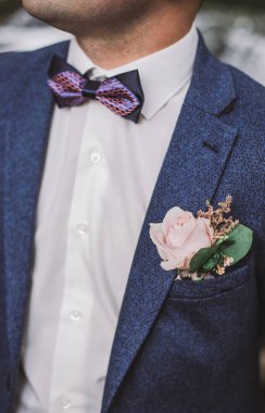 Mavi takım, beyaz gömlek, papyon ve yaka çiçeği yakışıklı damat yakın çekim dikey renkli görüntü.