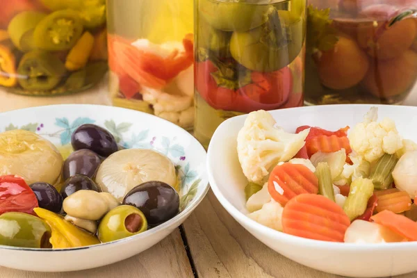 Close up of bowl with mixed vegetables in sunflower oil, bowl with marinated mixed vegetales  and glass jars with pickled vegetables on the background.