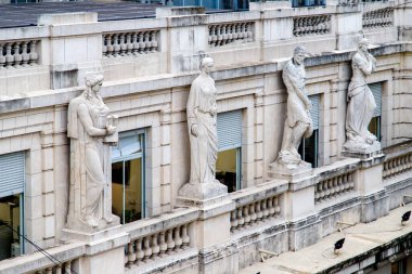 Beyaz taştan bir binanın dekoratif çatı cephesindeki neoklasik heykeller..