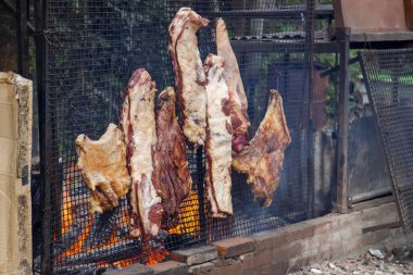 Dikey metal bir ızgarada açık ateşte büyük sığır eti kesikleri.