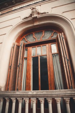 Kemerli ahşap pencereler, açık panjurlar ve klasik bir binanın ön cephesinde denge.