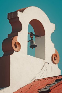 Beyaz ve turuncu bir kaplama içinde asılı küçük bir çanın yakın plan görüntüsü.