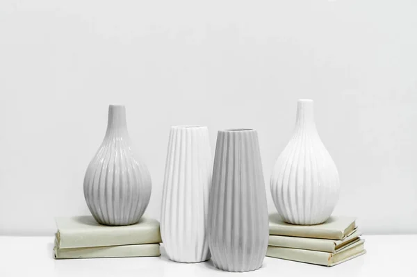 four vases on books; vases with books on a gray background; two white and two gray vases; vases with a narrow and wide neck; four empty vessels