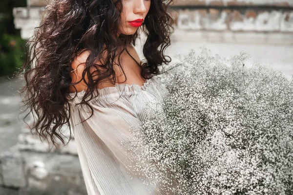 curly girl in sundress with lush bouquet posing against a light wall background