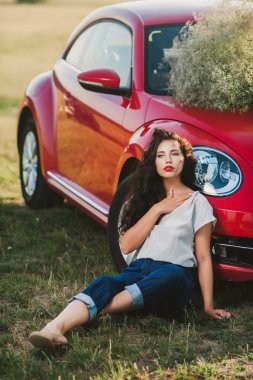 gün batımında kırmızı araba yakınındaki şortlu kıvırcık kız