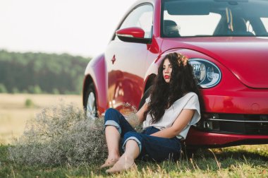 gün batımında kırmızı araba yakınındaki şortlu kıvırcık kız