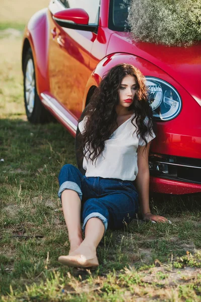 Kręcone Dziewczyna Krótkich Spodenkach Pobliżu Czerwony Samochód Zachodzie Słońca — Zdjęcie stockowe