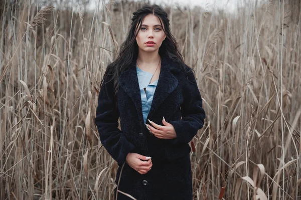 Kürk mantolu kız kuru sazlıkların arasında duruyor.