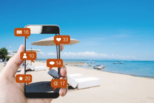 そしてソーシャル メディア ソーシャル ネットワークの通知アイコンとのビーチで手モバイル スマート フォン — ストック写真