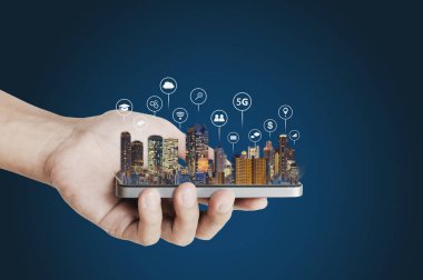 Hand holding mobile smart phone with buildings hologram and technology icons. Smart city, 5g, internet, blockchain technology, and networking technology concept