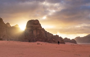 Gün doğumunda Wadi Rum çölünün manzarası tek başına yürüyen bir adamla ve taş dağın içinden güneş ışığıyla. Çölde seyahat ve maceracı, Ürdün