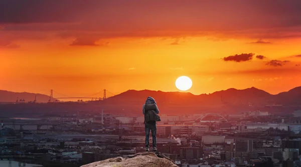 大阪市内の美しい夕日を楽しむ山の上に立つバックパックを持つ男 アジアでの旅行と冒険 — ストック写真