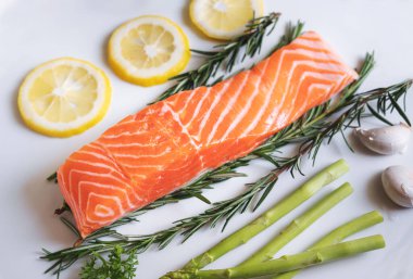 Çiğ somon fileto, bitkiler ve malzemelerle birlikte, beyaz tabakta.