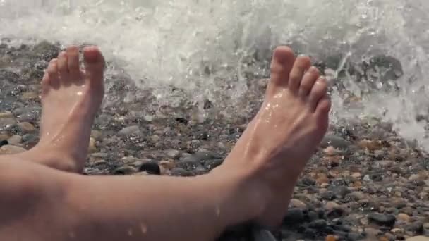A close-up of a childs legs is overwhelmed by a wave. Pebble sea beach  noisy sea waves on childrens legs
