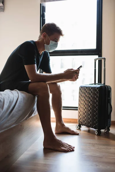 Грустный мужчина дома с телефоном и чемоданом и ждет открытия аэропорта Стоковая Картинка
