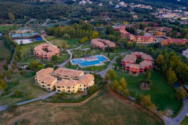 Lüks Yunan Adası Tatil Köyü: Büyük bir yüzme havuzu, birden fazla otel binası ve huzurlu bir ortamda yemyeşil bir çevreye sahip nefes kesici bir tatil beldesinin havadan görünüşü.