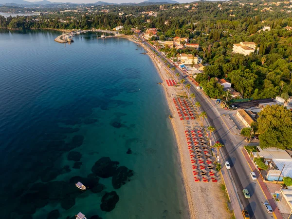 Aerial view of a coastal town with beach umbrellas, calm turquoise sea, boats on the water, seaside road, summer vacation destination, Mediterranean coastline, tranquil holiday travel landscape