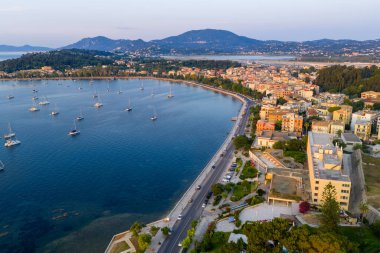 Yunanistan 'ın Korfu kentindeki Garitsa Körfezi' nin panoramik hava manzarası, yelkenliler ve kıyı yolu binalarla dolu.